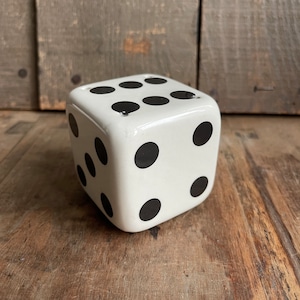 May include: A white ceramic dice with black dots. The dice is a home decor item.