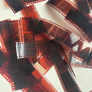 May include: A pile of old, used, clear plastic 35mm film negatives. The negatives are stacked on top of each other and are slightly overlapping. The negatives are all different sizes and shapes.