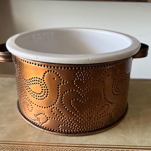 May include: A copper serving bowl with a white ceramic liner. The bowl has a decorative pattern of birds and swirls.