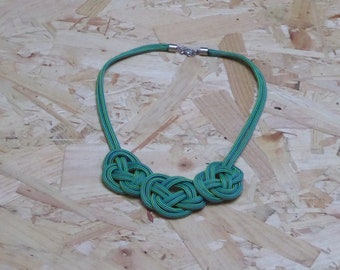 May include: A green and yellow striped necklace with three large knots. The necklace is made of a woven cord.