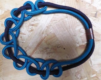 May include: A blue and black rope necklace with a metal clasp. The rope is knotted into a decorative pattern.