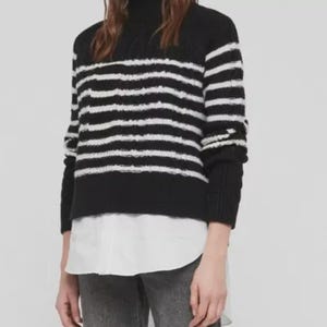 Pu&ograve; includere: Outfit da donna con maglione a righe bianche e nere, camicia bianca con colletto, jeans grigi e stivali neri con tacco. I jeans hanno gamba dritta e orlo grezzo.