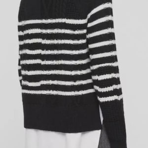 Pu&ograve; includere: Un maglione a righe bianche e nere con collo alto. Il maglione presenta un design a maglia strutturata e una camicia bianca che spunta da sotto. Le maniche sono lunghe e lo stile &egrave; casual.