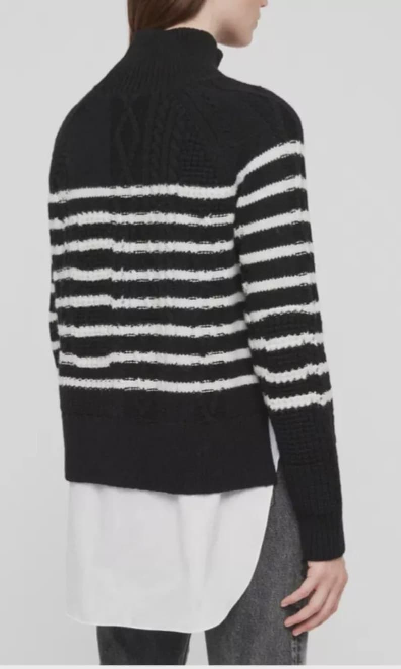 Pu&ograve; includere: Un maglione a righe bianche e nere con collo alto. Il maglione presenta un design a maglia strutturata e una camicia bianca che spunta da sotto. Le maniche sono lunghe e lo stile &egrave; casual.