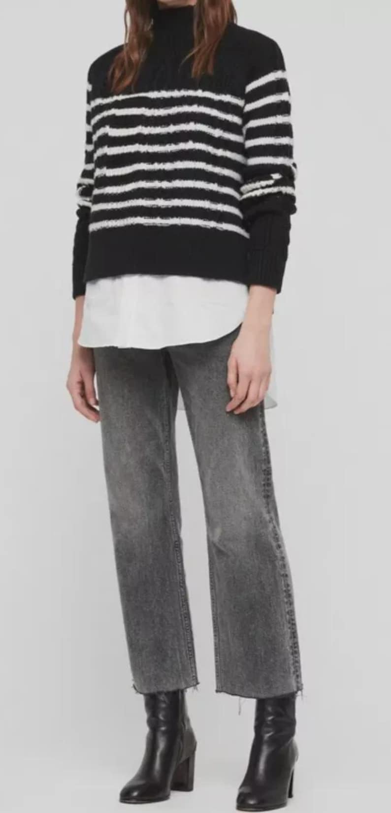 Pu&ograve; includere: Outfit da donna con maglione a righe bianche e nere, camicia bianca con colletto, jeans grigi e stivali neri con tacco. I jeans hanno gamba dritta e orlo grezzo.