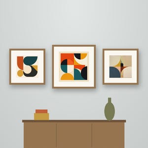 May include: Three framed square wall art prints featuring geometric quadrant circle patterns in orange, teal, and cream. The text reads Crestline Color Co. Quadrant Circle. Below, a brown sideboard holds a small box and a green vase.