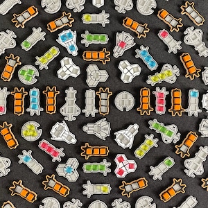 Może przedstawiać: Kolekcja kolorowych, geometrycznych elementów przypominających płytki, o różnych kształtach i wzorach. Płytki wykonane są z białego materiału z kolorowymi akcentami. Płytki są ułożone w okrągły wzór na ciemnoszarym tle.