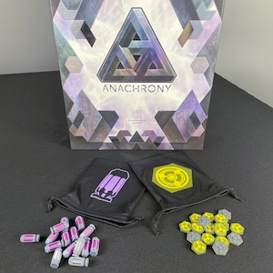 May include: A box for the board game "Anarchy" with a purple and grey geometric design. The box is open and shows two small black bags with symbols on them. One bag has a purple symbol of a capsule and the other has a yellow symbol of a gear. There are also small purple and grey tokens on the table.