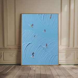 May include: A framed art print featuring a textured, light blue background with a wave-like pattern. Several small figures are depicted surfing on the waves. The artwork is displayed in a room with wood flooring and beige walls.