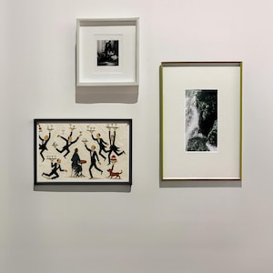 May include: Three framed wall art pieces displayed on a plain wall. The top left is a square black and white photograph, the bottom left is a rectangular illustration of waiters serving a seated figure, and the right is a vertical black and white print.