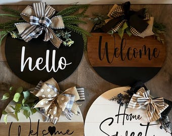 May include: Four round wooden signs with different welcome messages and decorative bows. The signs read "hello", "welcome", "welcome to our home", and "home sweet home".
