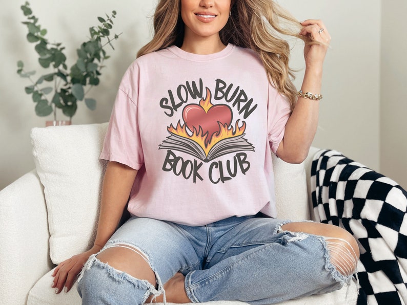 May include: A pink t-shirt with the text "Slow Burn Book Club" and a graphic of a book with a heart on fire.