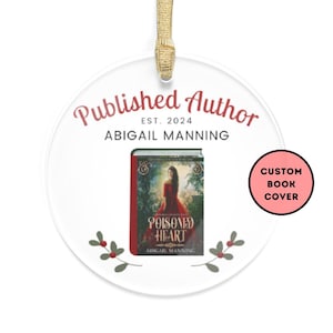 May include: Round white ornament with a red and green holly design. The ornament features the text "Published Author Est. 2024 Abigail Manning" and a book cover with the title "Poisoned Heart" by Abigail Manning. The ornament also includes a red circle with the text "Custom Book Cover".