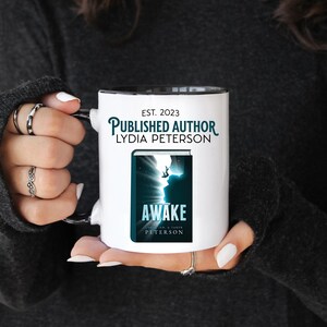 May include: White ceramic mug with a black rim and handle. The mug features the text "EST. 2023 PUBLISHED AUTHOR LYDIA PETERSON" and a book cover with the title "AWAKE" and the author's name.