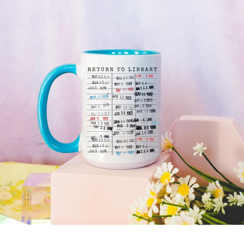 Puede incluir: Taza de cer&aacute;mica blanca con interior y asa azules. La taza presenta un dise&ntilde;o impreso que se asemeja a una tarjeta de biblioteca, con las palabras "RETURN TO LIBRARY" y varias fechas. Margaritas y una forma geom&eacute;trica en el fondo.