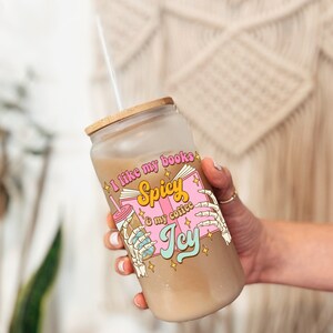 Pu&ograve; includere: Un bicchiere di vetro trasparente con un coperchio in bamb&ugrave; e una cannuccia. Il bicchiere ha una grafica rosa e gialla che dice "Mi piacciono i miei libri piccanti e il mio caff&egrave; ghiacciato".