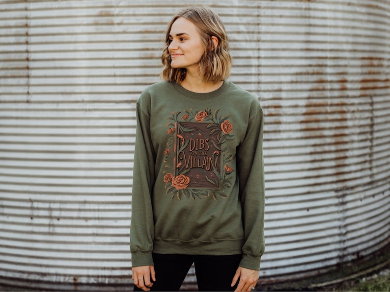 May include: A green sweatshirt with a floral design and the text "Dibs on the Villain" printed on the front.