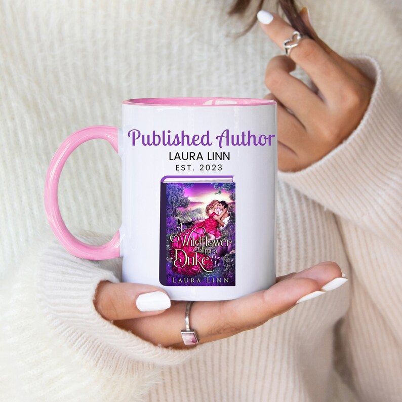 May include: White ceramic mug with a pink handle and interior. The mug features the text "Published Author" and "LAURA LINN EST. 2023". The mug also displays a book cover image titled "A Wildflower for the Duke" by Laura Linn.