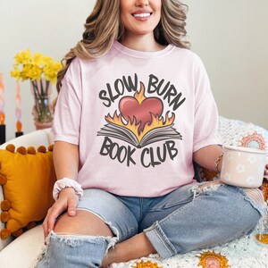 May include: A pink t-shirt with the text "Slow Burn Book Club" and a graphic of a book with a heart on fire.