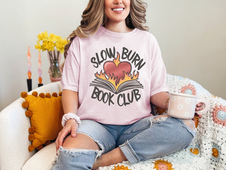 May include: A pink t-shirt with the text "Slow Burn Book Club" and a graphic of a book with a heart on fire.