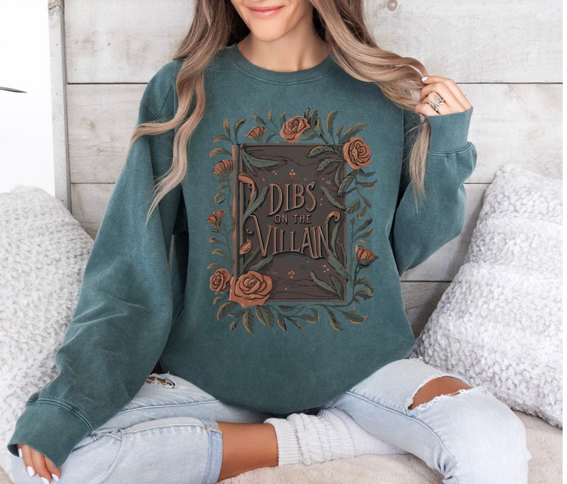 May include: Teal sweatshirt with a floral design and the text "Dibs on the Villain" printed on the front.