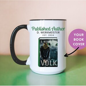 May include: White ceramic mug with a black handle and rim. The mug features a book cover design with the title "VOLK" and the author's name, D. Werkmeister. The mug also has the text "Published Author" and "EST. 2024".