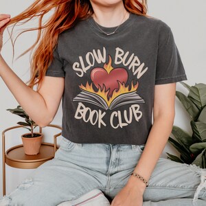 May include: A black cropped t-shirt with a graphic of a heart on fire with a book underneath. The text "Slow Burn Book Club" is printed on the shirt.