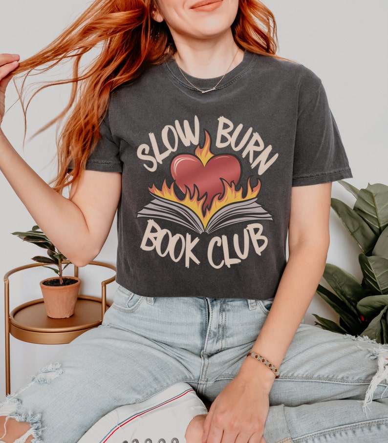 May include: A black cropped t-shirt with a graphic of a heart on fire with a book underneath. The text "Slow Burn Book Club" is printed on the shirt.