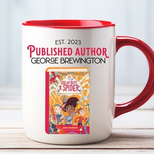 May include: White ceramic mug with a red rim and handle. The mug has the text "EST. 2023 PUBLISHED AUTHOR GEORGE BREWINGTON" printed on the front. Below the text is an illustration of a book cover with the title "The Girl Who Built a Spider" and the author's name.