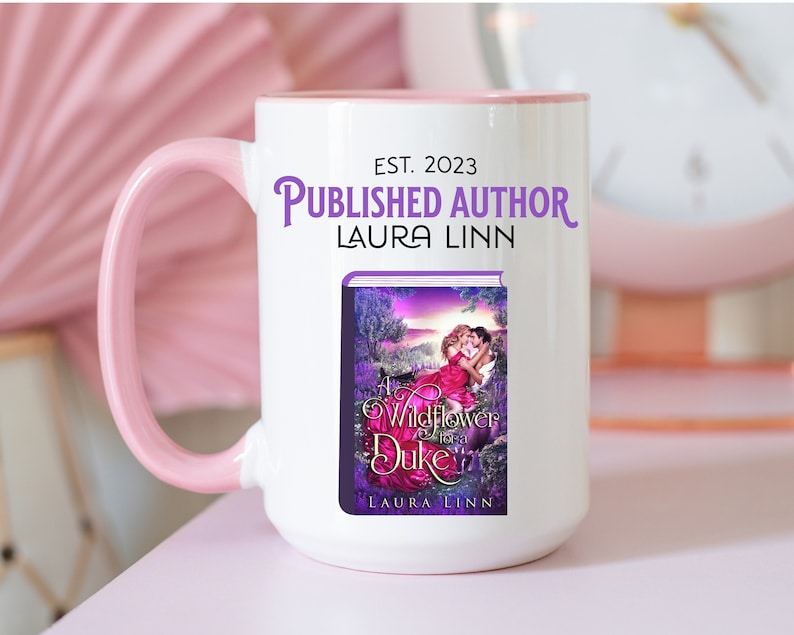 May include: White ceramic mug with a pink handle and rim. The mug features the text "EST. 2023 PUBLISHED AUTHOR LAURA LINN" and a book cover with the title "A Wildflower for a Duke" by Laura Linn.