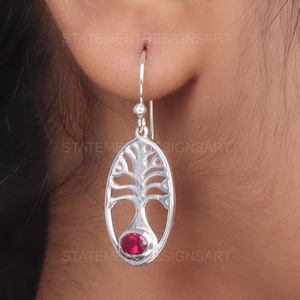 Könnte beinhalten: Silberne Lebensbaum-Ohrringe mit einem rosafarbenen Edelstein in der Mitte.