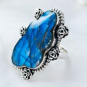 May include: A silver ring with a large blue labradorite gemstone set in a floral design. The ring is adorned with small silver flowers around the gemstone.