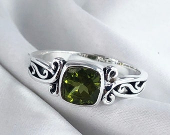 May include: A silver ring with an ornate design features a square green gemstone.