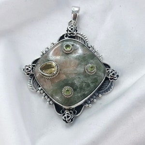 May include: A silver pendant with a large, square-shaped, green and pink stone. The pendant is adorned with smaller green and yellow gemstones, and decorative floral and leaf accents. The pendant has a bail for a chain.
