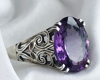 May include: A silver ring featuring an oval amethyst gemstone set in a filigree design.