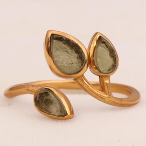 Può includere: Un anello color oro con tre gemme verdi a forma di goccia, disposte a forma di foglie. Il design dell'anello è ispirato alla natura, con le gemme incastonate in una fascia dorata.