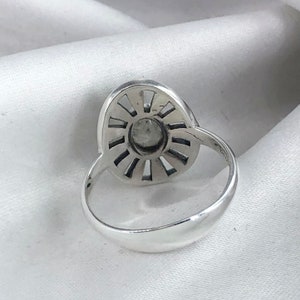 May include: A silver ring featuring a large, oval-shaped stone set within a sunburst design. The stone is encircled by a ring of smaller stones.