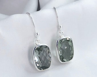 Puede incluir: Un par de pendientes de plata con gotas de piedras preciosas verdes. Las piedras preciosas son rectangulares y tienen un corte facetado.