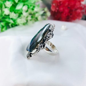 May include: A silver ring with a large, dark green, oval-shaped gemstone. The ring is decorated with small, silver roses around the gemstone.