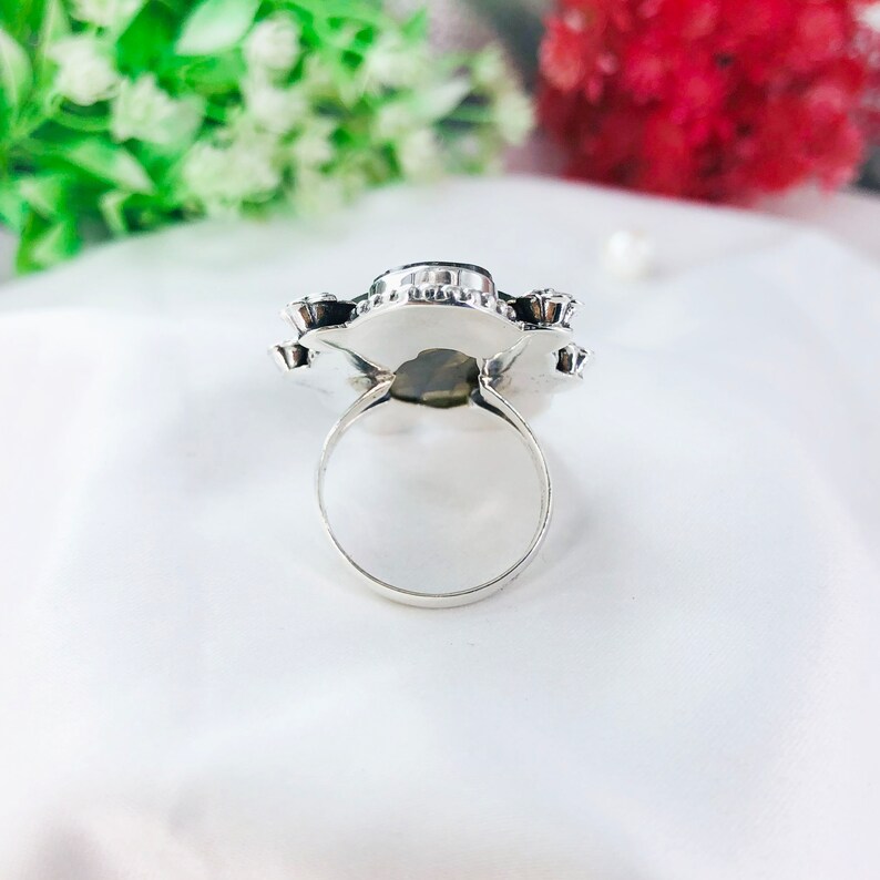 May include: A silver ring with a large, dark green gemstone set in a flower-shaped design.