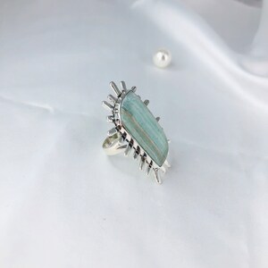 K&ouml;nnte beinhalten: Ein silberner Ring mit einem gro&szlig;en, rechteckigen, hellblauen und gr&uuml;nen Edelstein, der in einem Sternendesign gefasst ist.