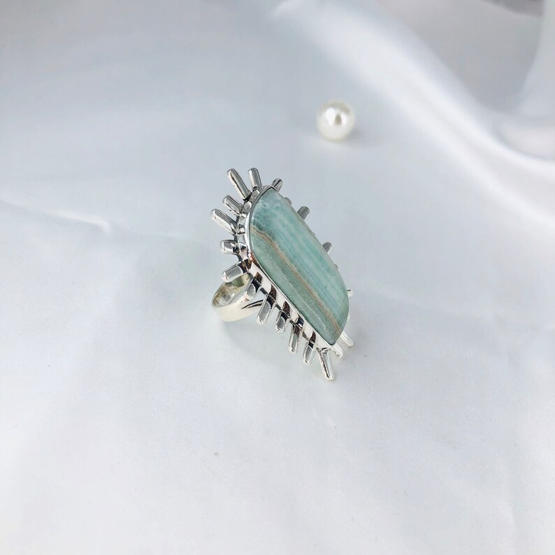 K&ouml;nnte beinhalten: Ein silberner Ring mit einem gro&szlig;en, rechteckigen, hellblauen und gr&uuml;nen Edelstein, der in einem Sternendesign gefasst ist.