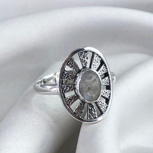 May include: A silver ring featuring a moonstone set within a sunburst design.