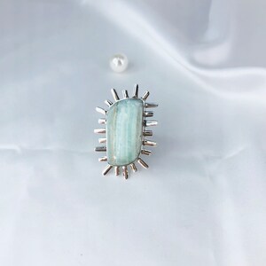 K&ouml;nnte beinhalten: Ein silberner Ring mit einem hellblauen Aquamarin-Stein, der in einem Sonnenstrahl-Design gefasst ist.