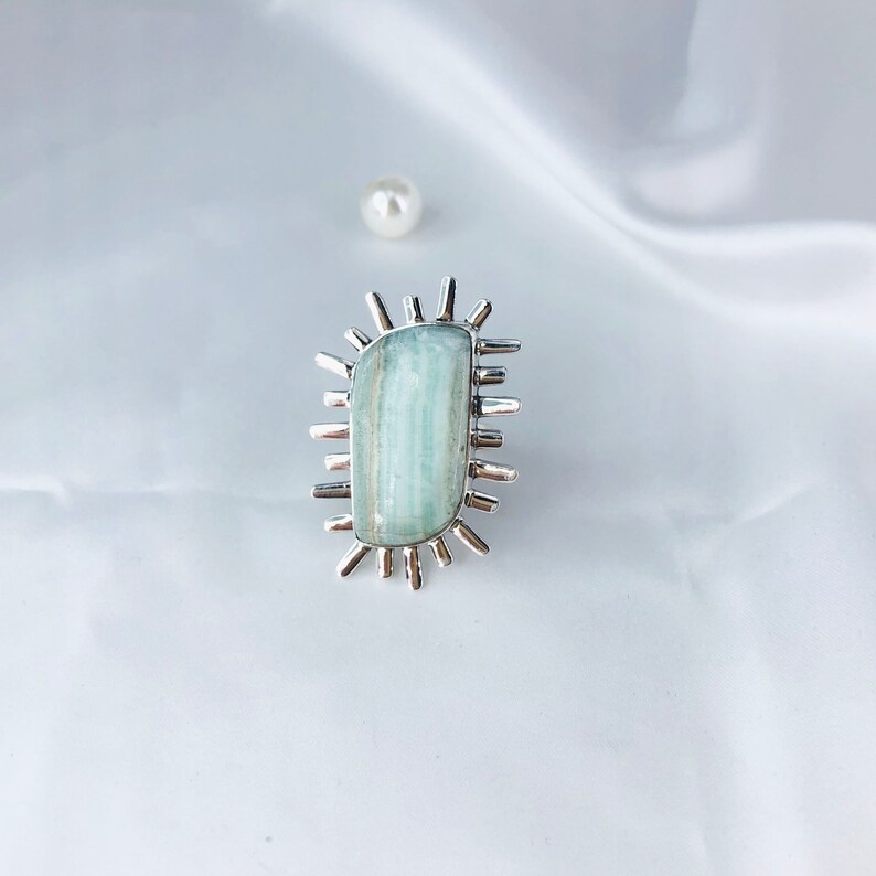 K&ouml;nnte beinhalten: Ein silberner Ring mit einem hellblauen Aquamarin-Stein, der in einem Sonnenstrahl-Design gefasst ist.