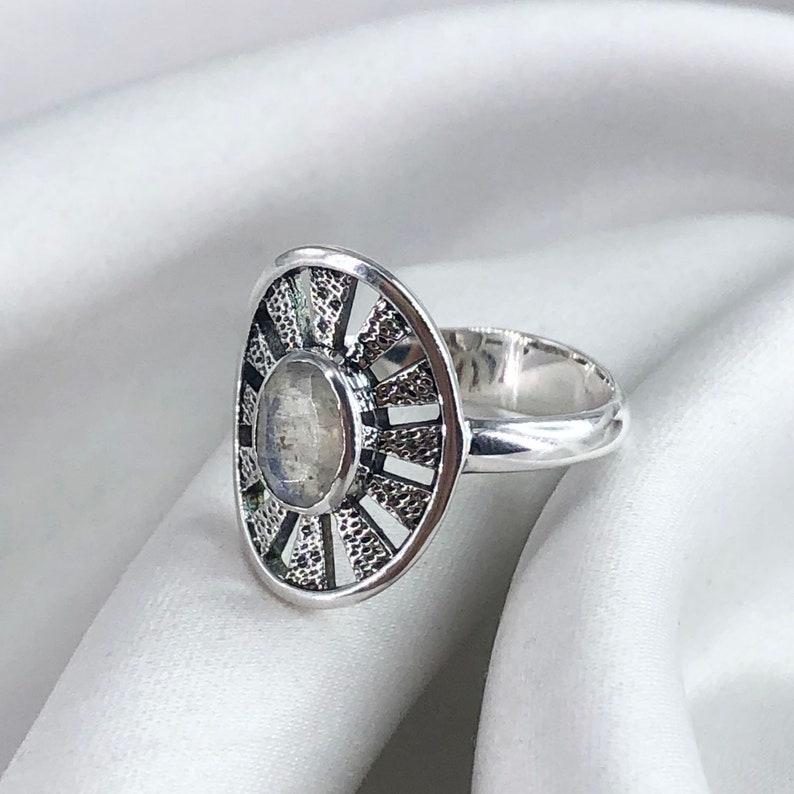 May include: A silver ring featuring a moonstone set within a circular design. The ring has a delicate, intricate pattern surrounding the stone.