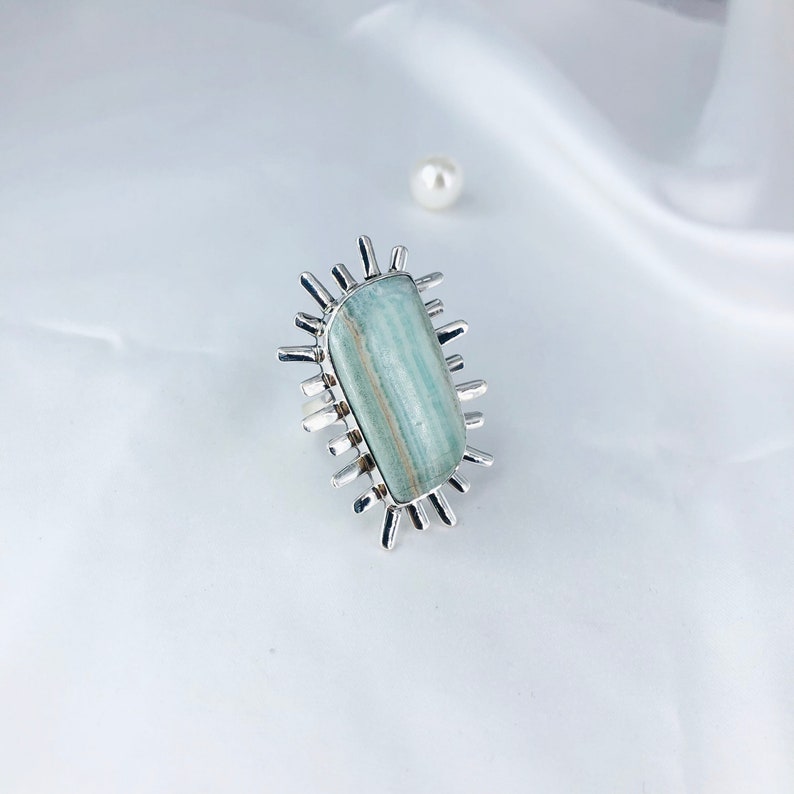 May include: A silver ring with a light blue and green gemstone set in a starburst design.