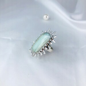 K&ouml;nnte beinhalten: Ein silberner Ring mit einem hellblauen Aquamarin-Edelstein, der in einem Sternburst-Design gefasst ist.