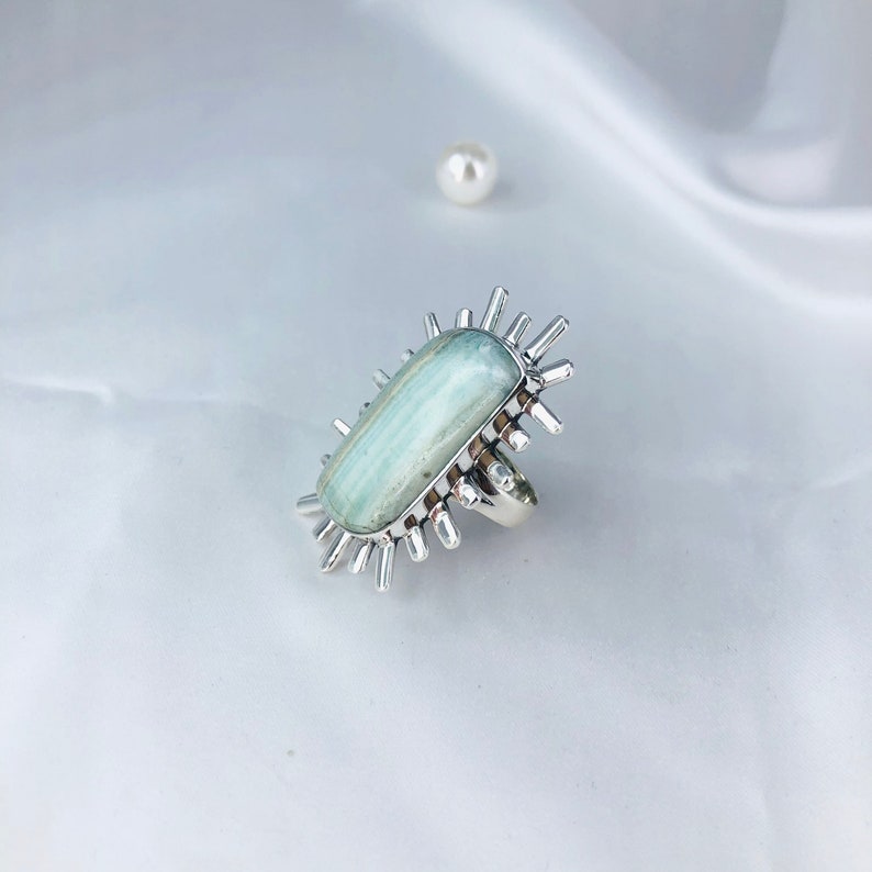 K&ouml;nnte beinhalten: Ein silberner Ring mit einem hellblauen Aquamarin-Edelstein, der in einem Sternburst-Design gefasst ist.