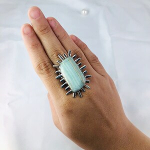 K&ouml;nnte beinhalten: Ein silberner Ring mit einem gro&szlig;en, rechteckigen, hellblauen Edelstein, der in einem Sternendesign gefasst ist.